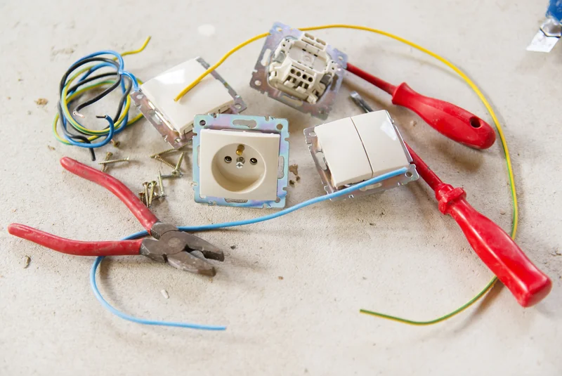 Pliers, screwdrivers, wire, an outlet and switch parts laid out for an outlet replacement in a Mason City home